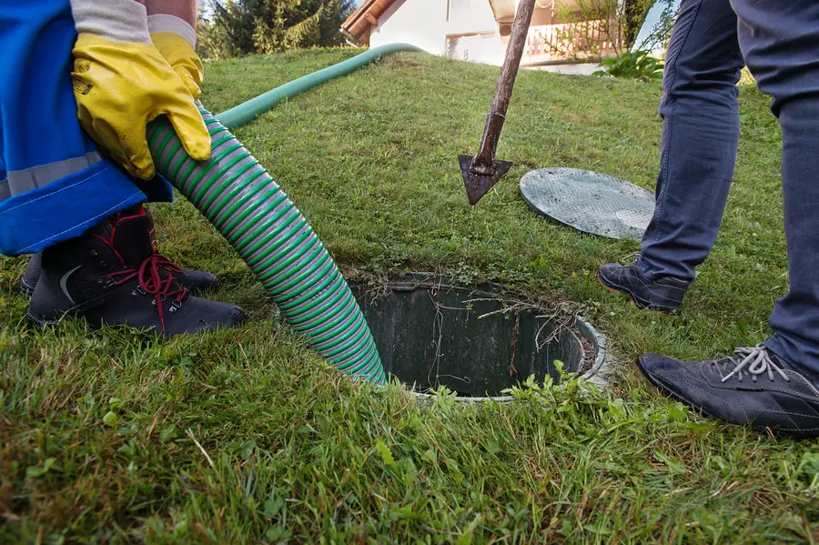 Tech feeding a vacuum hose into an open septic tank in a lawn
